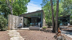 A modern house with a glass facade, stone walls, and a stone pathway leading to a seating area with a bench and a table. - Adults-Only Lake Peninsula Cottage w/ Pool, Pickleball & Sunset Views (Malakoff)