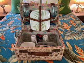 A wicker basket with a handle, containing a plate, two glasses, a mug, and a bottle. - Aloha Suite: Watch Whales, Breakfast included at Ala Kai Bed and Breakfast (Keaau)