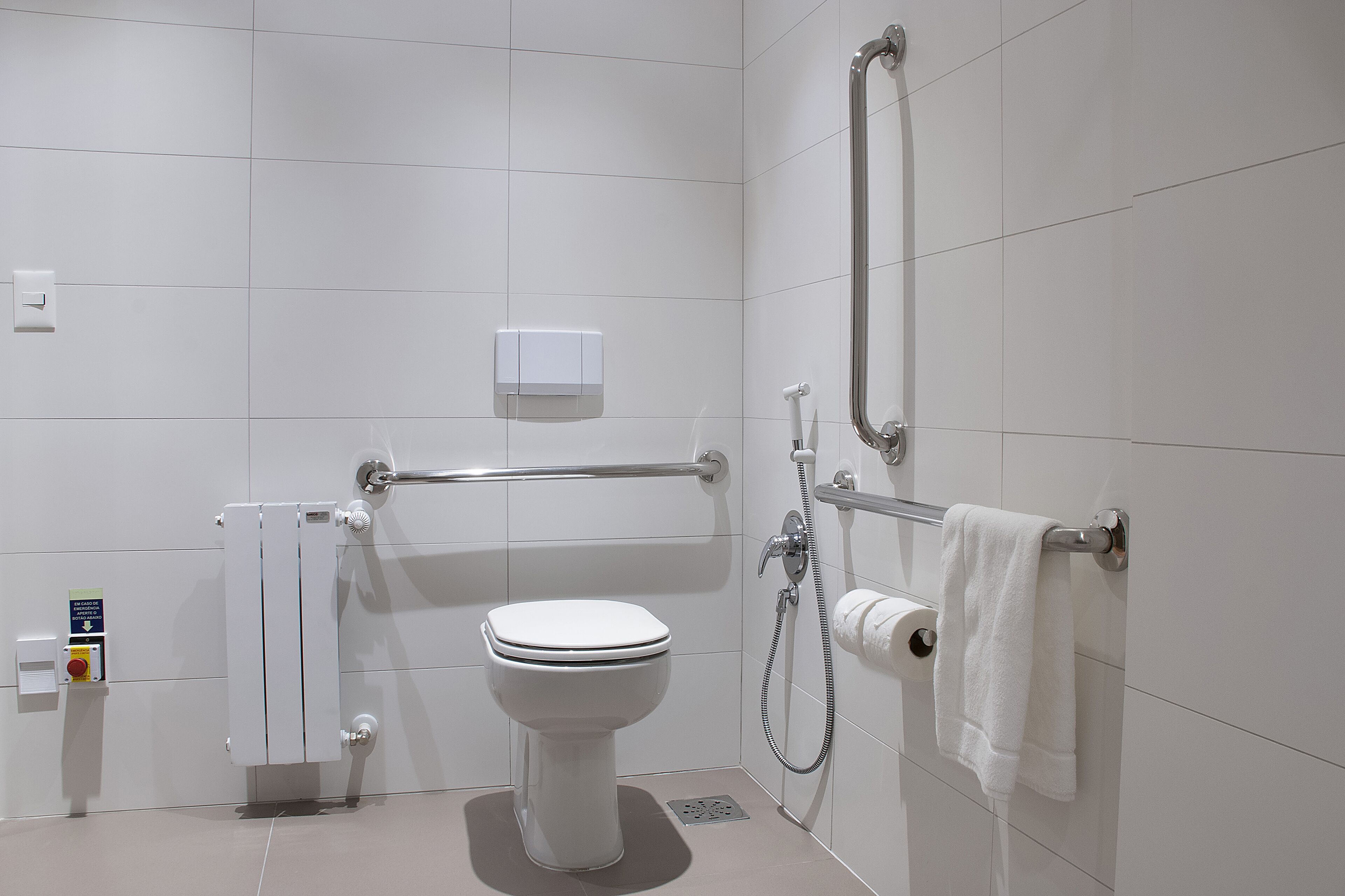 A modern bathroom with a toilet, hand dryer, towel rack, and a shower with a handheld showerhead.