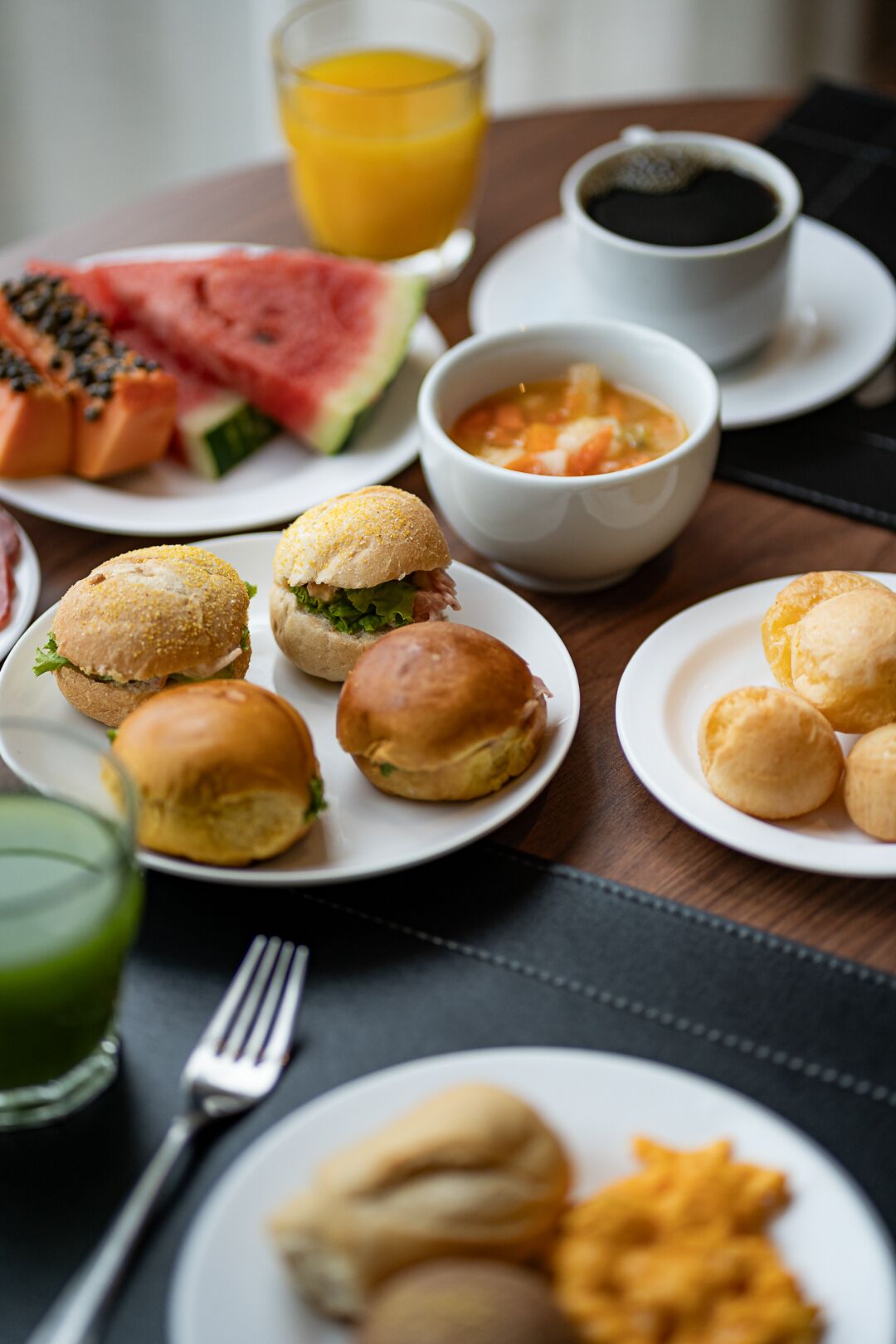 A breakfast setting with sandwiches, soup, watermelon, and juice.