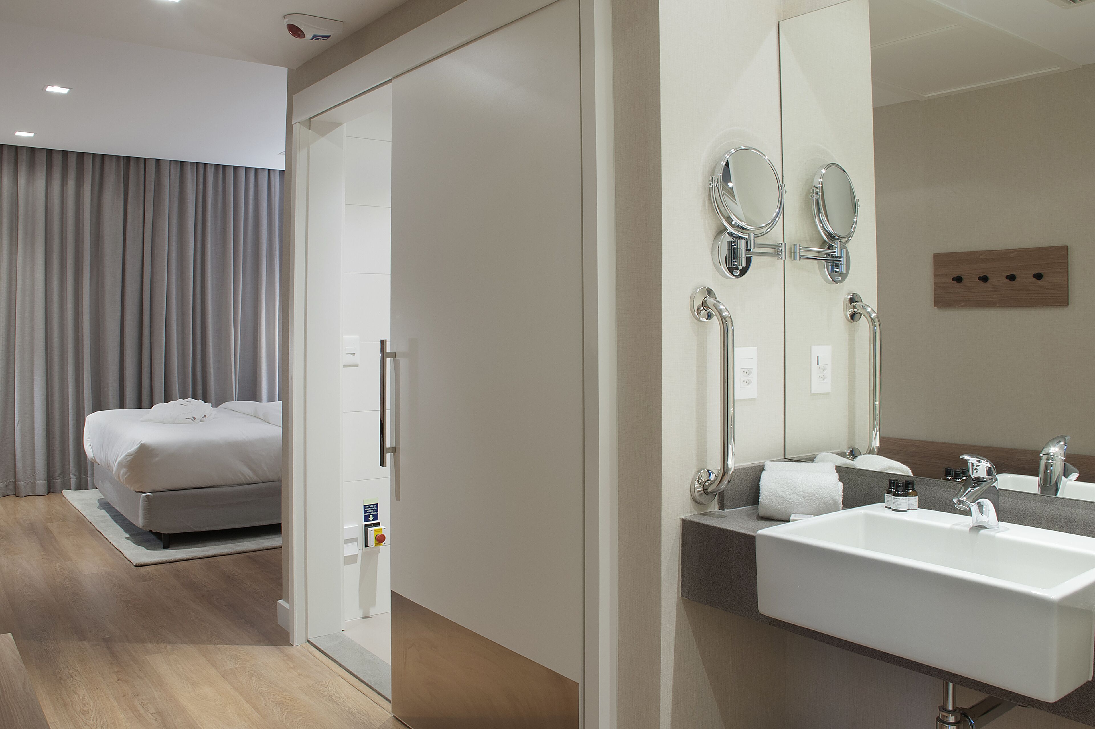 Una habitación de hotel moderna con una cama, un baño con un espejo grande y un lavamanos.