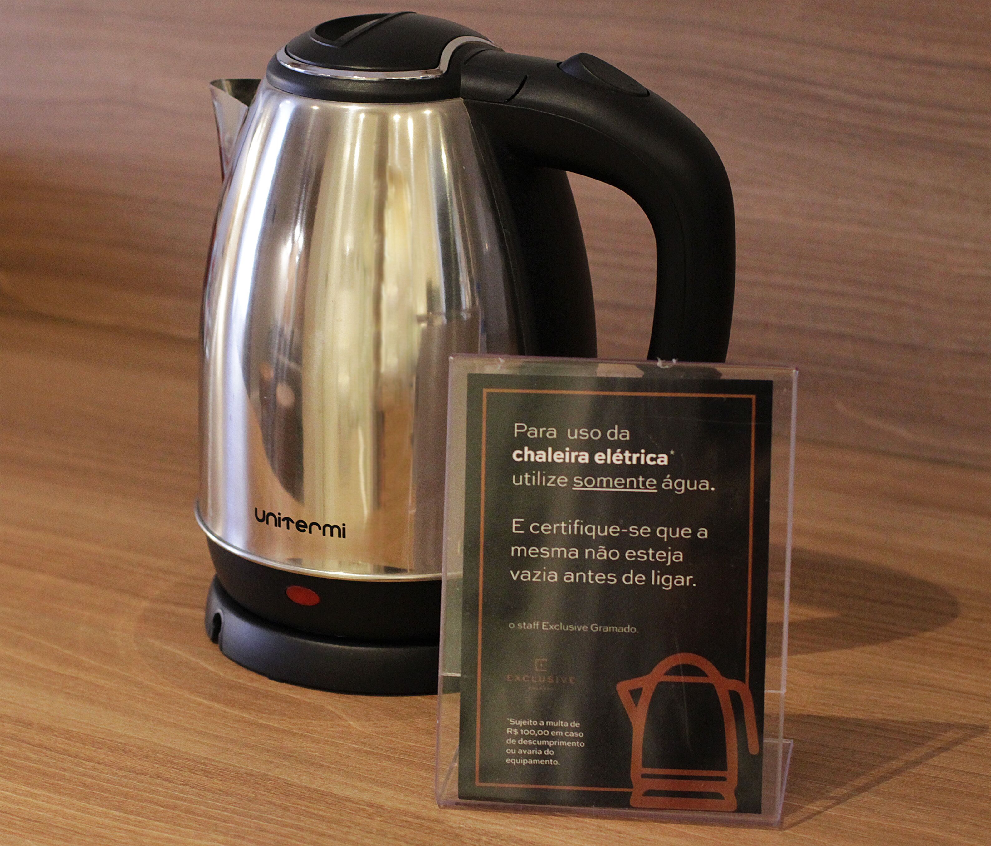 A stainless steel electric kettle with a black handle and a clear instruction sign beside it.