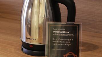 A stainless steel electric kettle with a black handle and a clear instruction sign beside it.