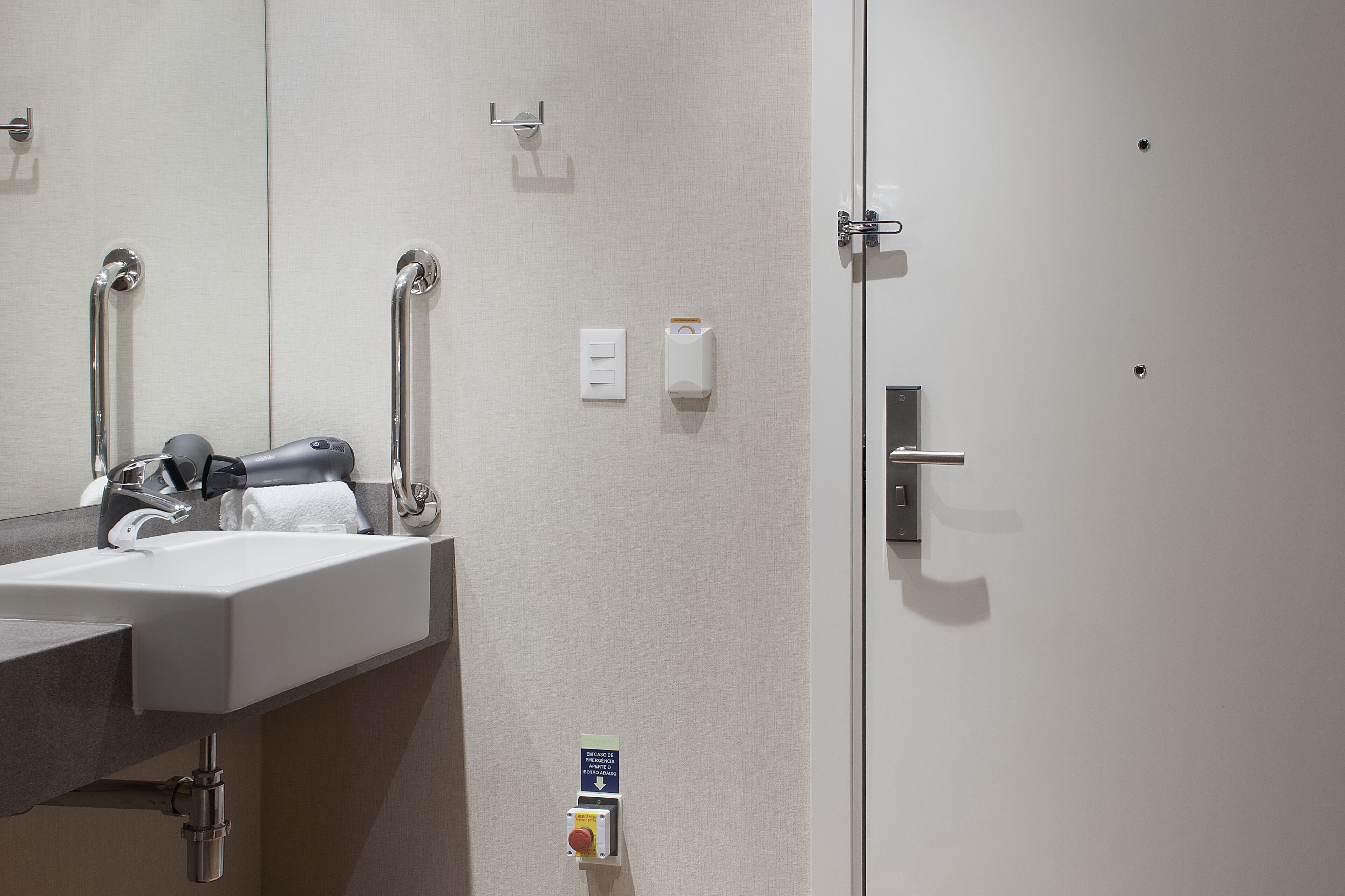 A bathroom with a sink, mirror, towel dispenser, and a door with a handle.