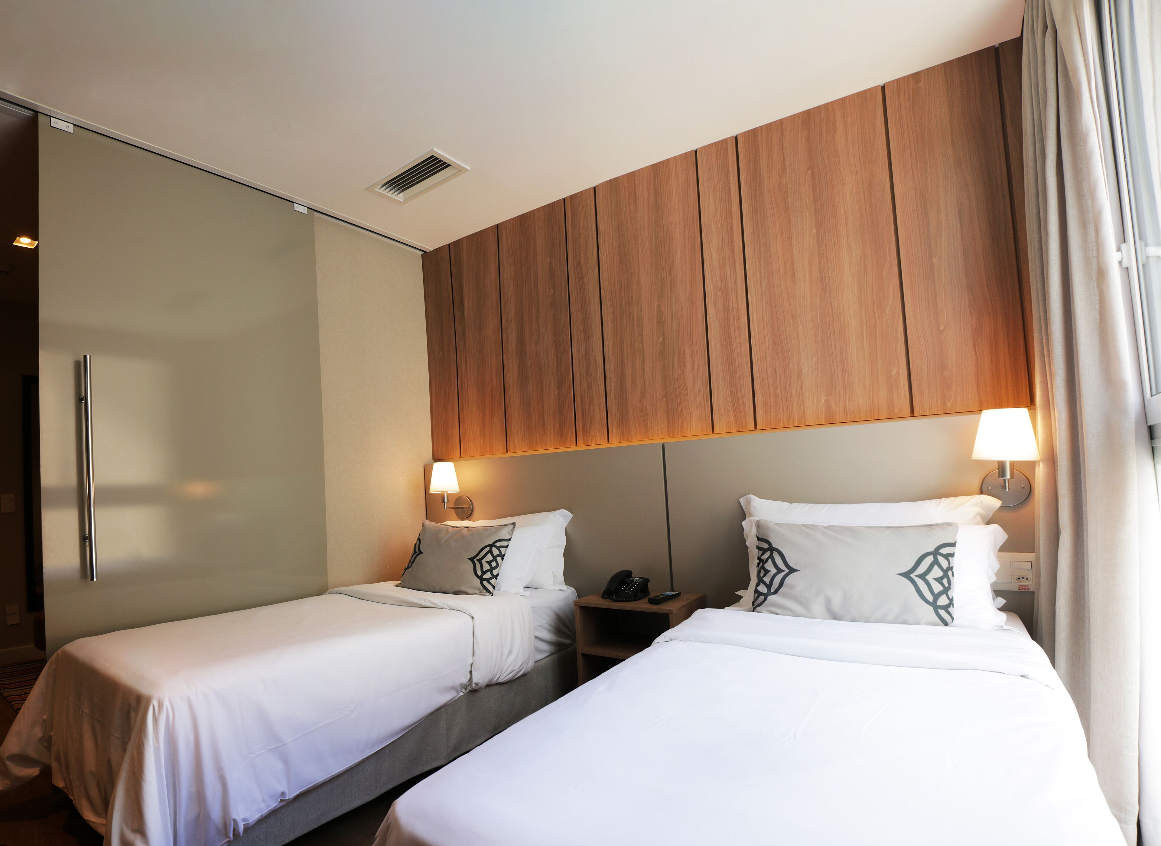 A hotel room with two single beds, a wooden headboard, bedside lamps, a telephone, and a wardrobe.