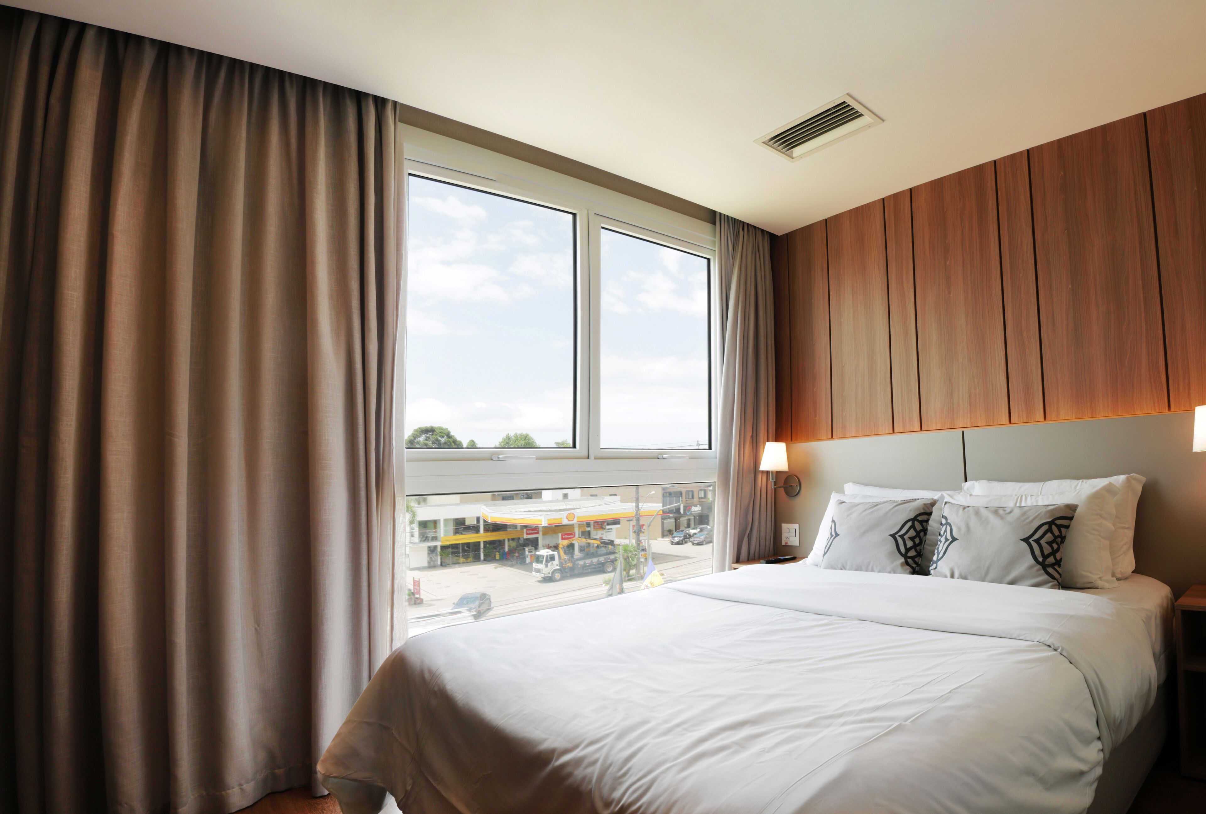 A hotel room with a large bed, a view of a gas station, and wooden paneling on the walls.