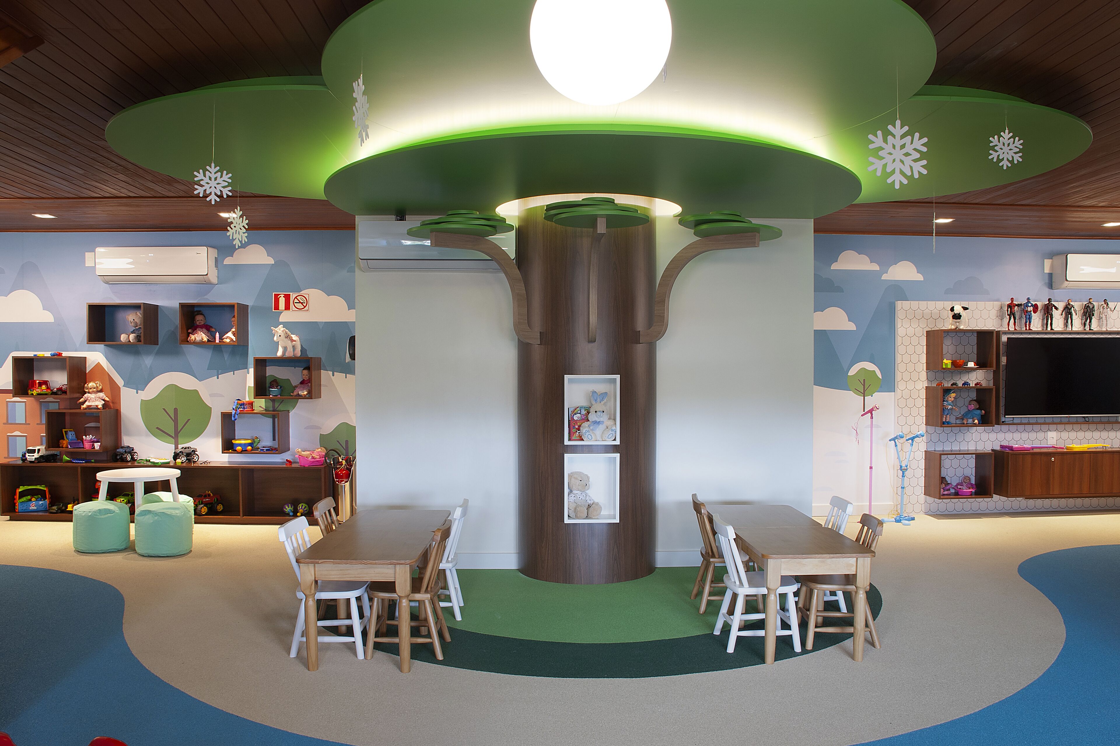 Un cuarto de juegos infantil con una estructura central en forma de árbol, asientos y zonas de juego.