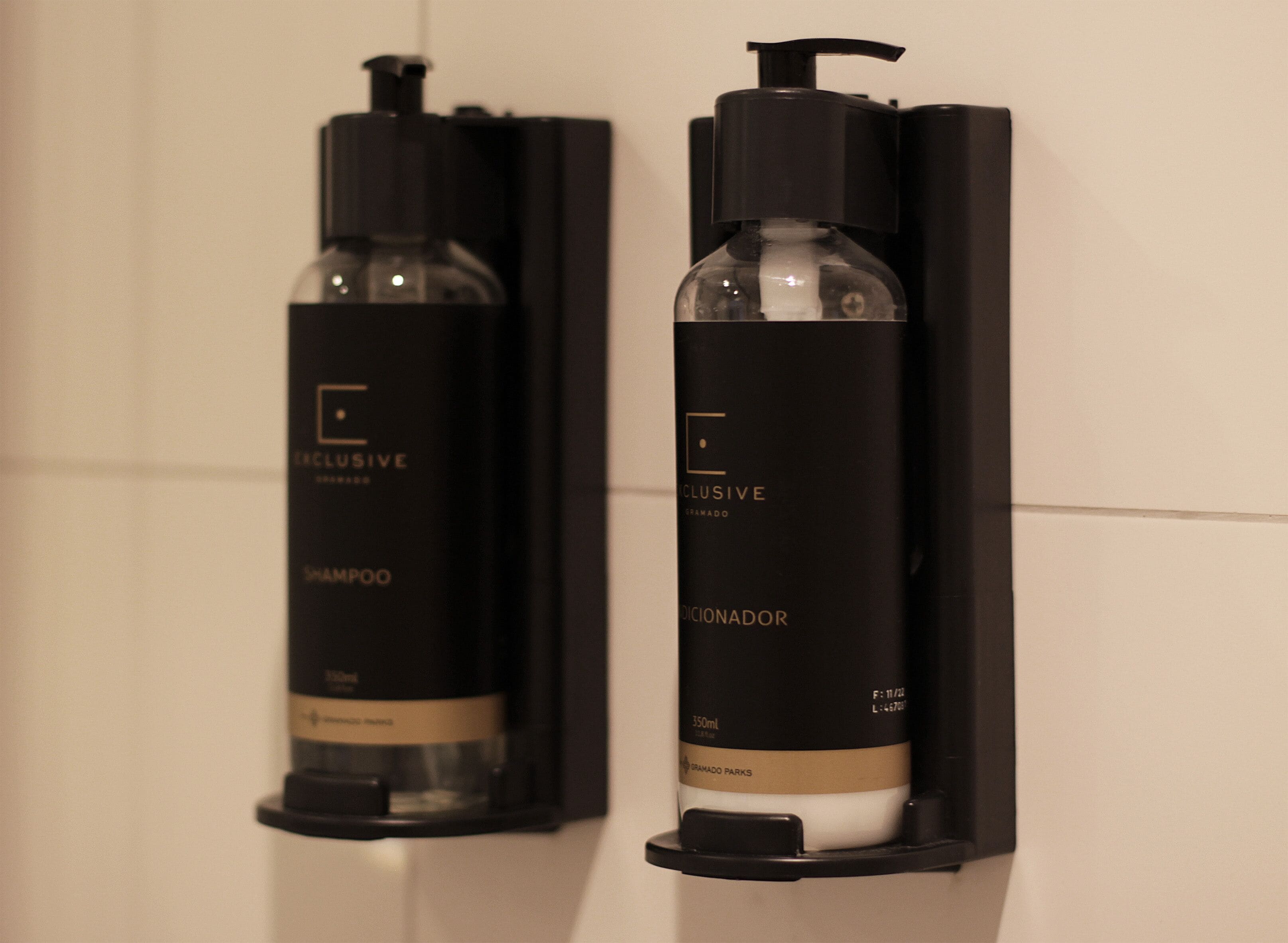 Två svarta flaskor med pumpar, varav den ena är märkt med texten ”SCHAMPO” och den andra med ”DEODORANT”, monterade på en vägg.