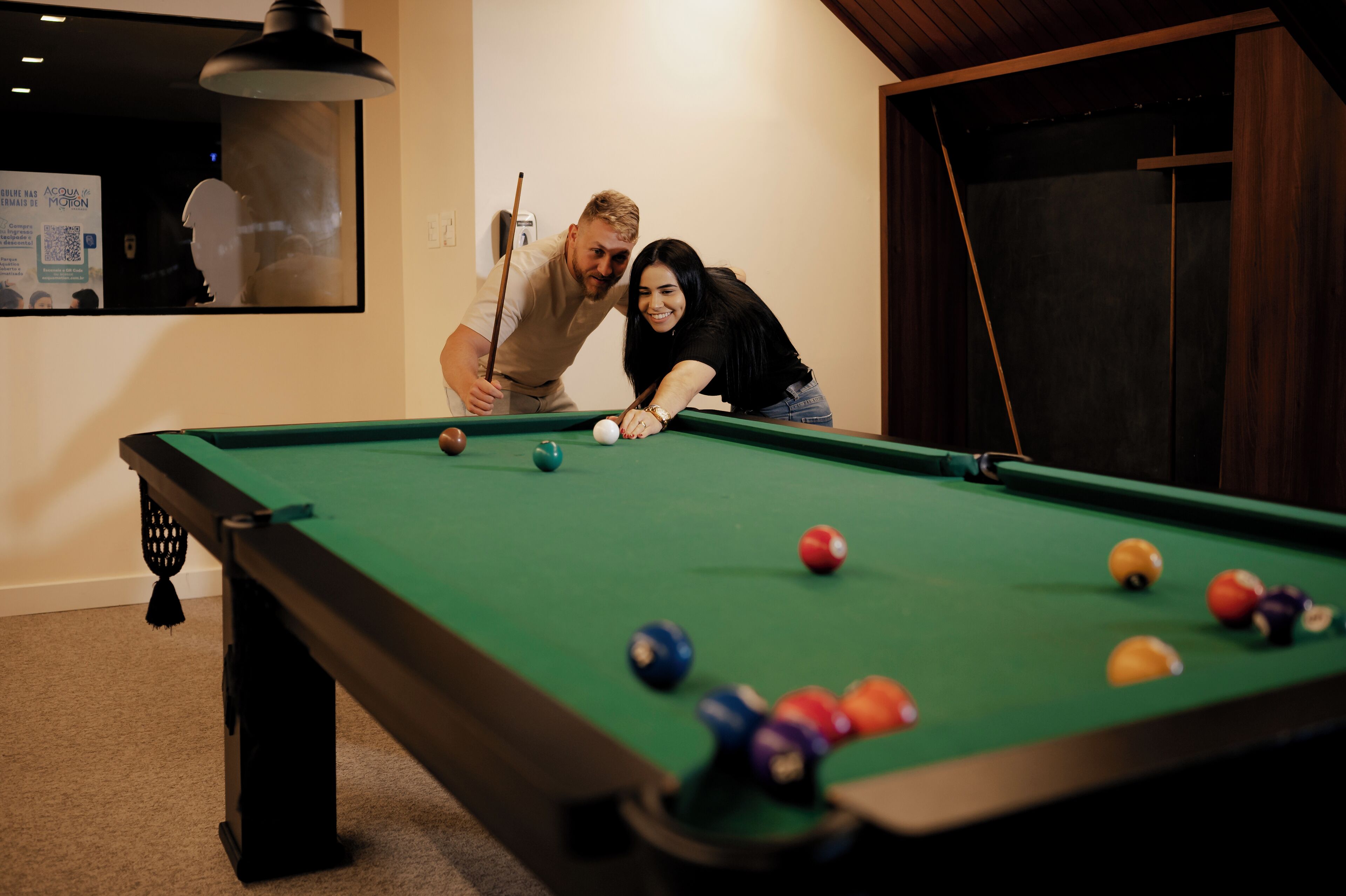 A pool table with balls, a person leaning over it, and a poster on the wall.