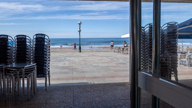 Eine Terrassengruppe am Strand mit gestapelten Stühlen und Tischen, mit Blick auf das Meer.