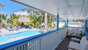 Ein Poolbereich mit blauer Liegefläche, Liegestühlen, einem Grill und Blick auf Gebäude im Hintergrund.