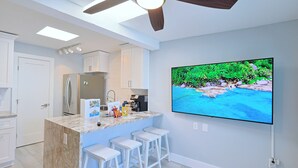 Eine moderne Küche mit einer zentralen Kochinsel, Barhocker, einem Deckenventilator und einem großen Fernseher, der an der Wand befestigt ist.