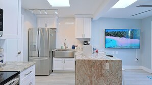 Eine moderne Küche mit einer großen Kochinsel, Edelstahlgeräten und einem an der Wand montierten Flachbildfernseher.