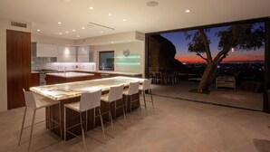 A modern kitchen with a central island, bar seating, and a view of the sunset through large windows.
