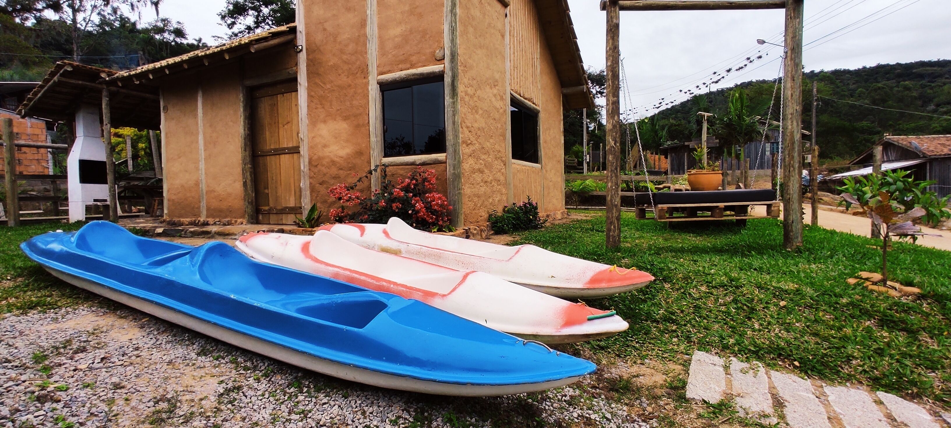 A rustic house with a porch, a blue and white boat, and a swing.