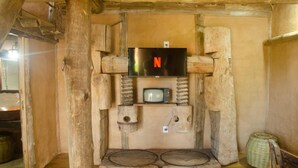 Una stanza rustica in legno con una televisione montata su una parete in pietra, un piccolo ripiano in legno sotto e un cesto di vimini sulla destra.