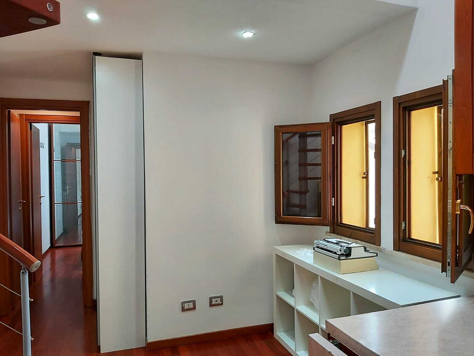 A narrow hallway with a wooden door, a white wall, and a shelf with a printer.