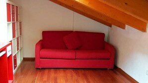 Un sofá rojo en una habitación con suelo de madera y techo inclinado.