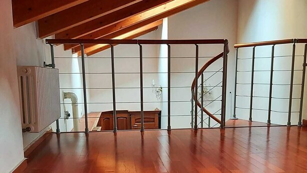 Una habitación en el ático con suelo de madera, una escalera y un radiador.
