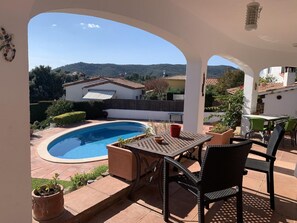 A patio with a pool, outdoor furniture, and a view of houses and hills.