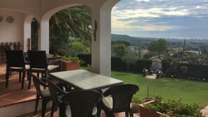 An outdoor patio with a table and chairs, surrounded by potted plants and a view of a cityscape. - Santet CostaBravaSi - Pool, BBQ, garden, wifi (Calonge)