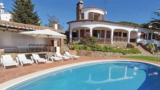A swimming pool with white lounge chairs and a white building with a curved roof in the background. - Santet CostaBravaSi - Pool, BBQ, garden, wifi (Calonge)