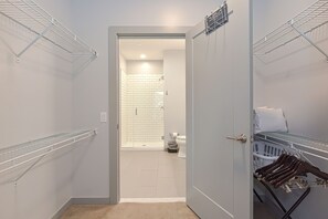 Un cuarto de lavandería con tendederos metálicos, una zona de ducha con azulejos blancos y una puerta que da a otra habitación.