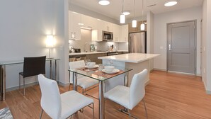 Une cuisine moderne avec des meubles blancs, des appareils en acier inoxydable et une table à manger en verre, assortie de chaises blanches.