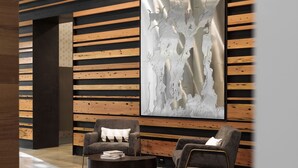 Un hall d’entrée moderne avec des panneaux de bois, deux fauteuils gris, une table basse ronde et une grande œuvre d’art abstraite accrochée au mur.