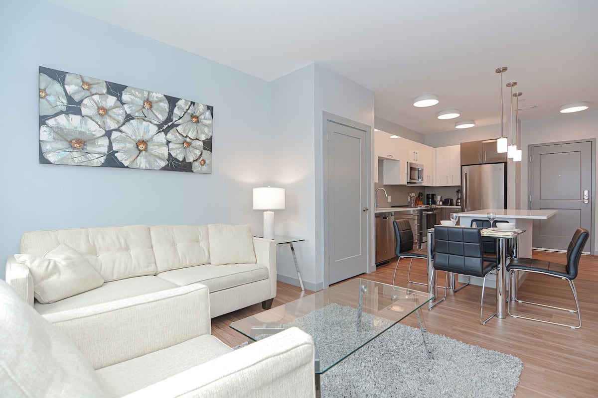 A modern living room with a sofa, a glass coffee table, and a dining area with chairs.