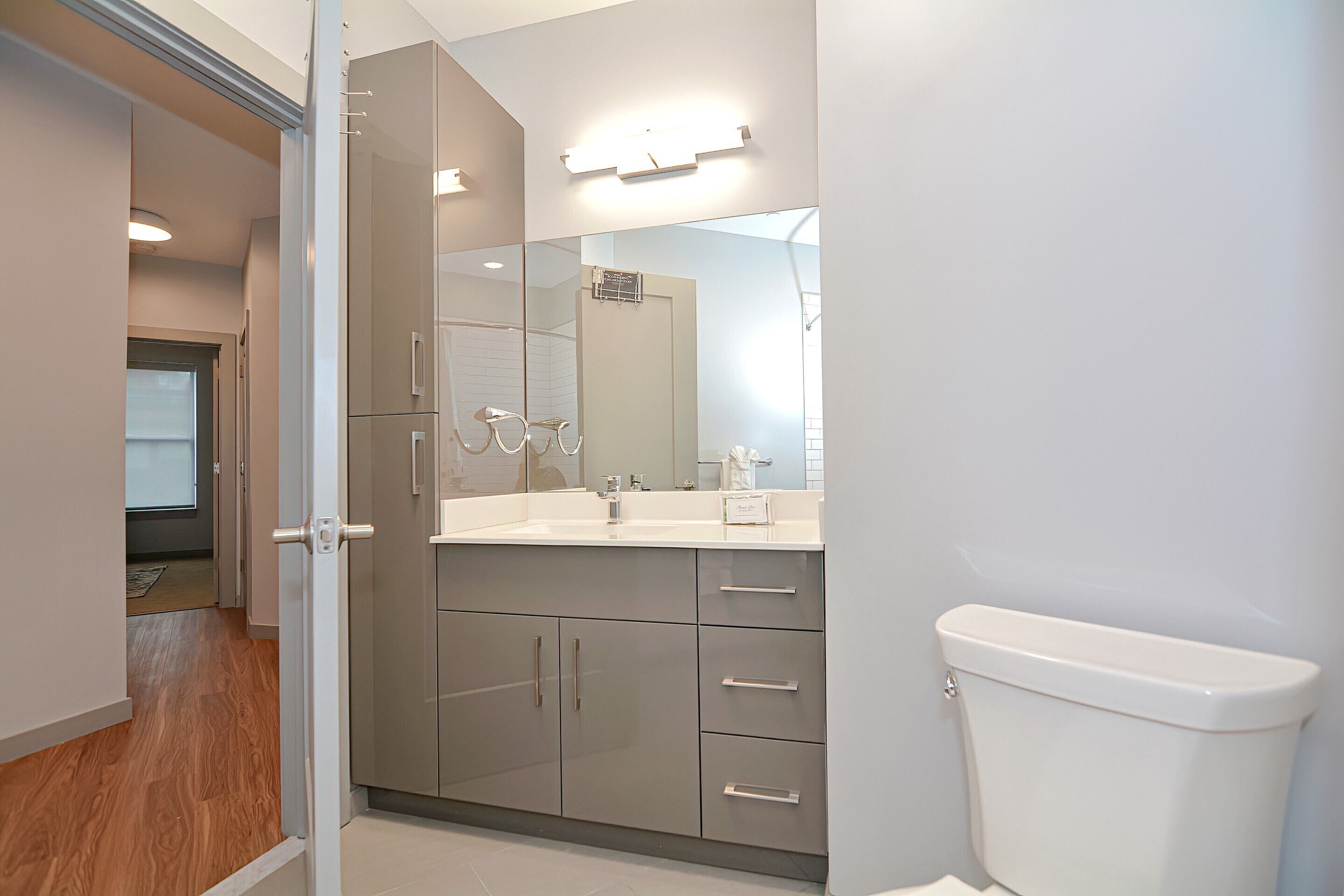 A modern bathroom with a large mirror, a white sink, and a toilet.