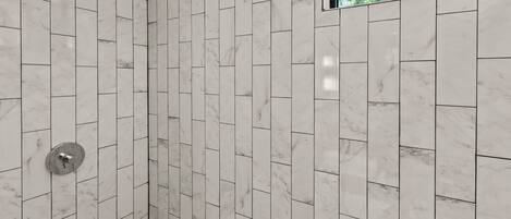 Une douche dont le carrelage est disposé en motif chevrons et une fenêtre donnant sur les arbres.