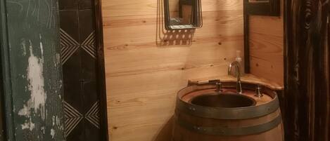 A wooden interior with a wooden door, a mirror, a sink with a wooden barrel, and a patterned wall.