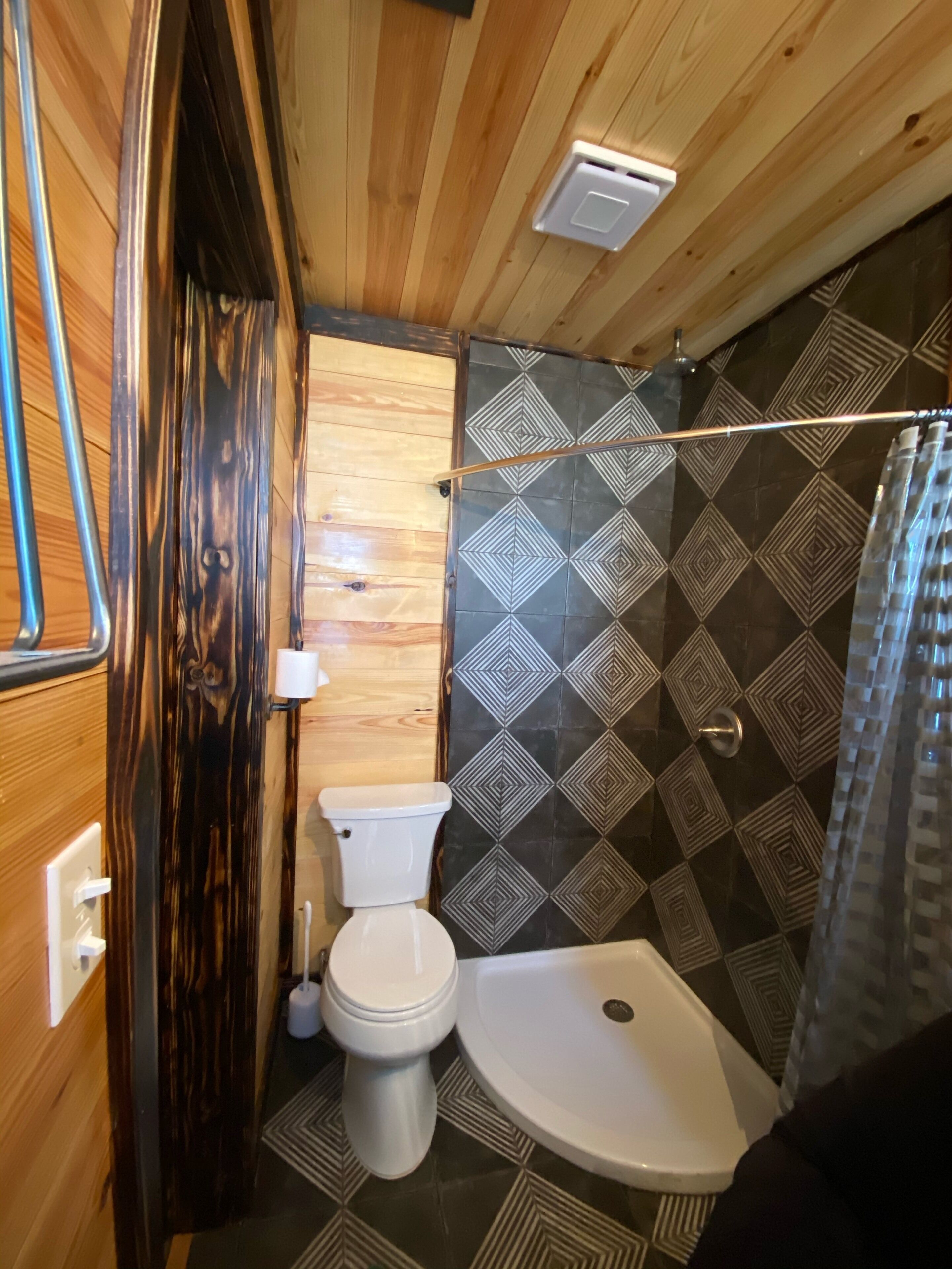 Une petite salle de bain comprenant des toilettes, une douche et un plafond en bois.