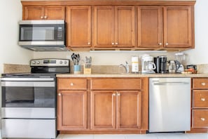 Cozinha com armários de madeira, micro-ondas, forno e máquina de lavar louça de aço inoxidável.