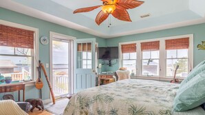 A bedroom with a large bed, a ceiling fan, a television, and a view of the outdoors. - Luney Dunes Penthouse (Newburyport)