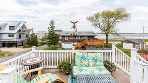 A residential area with a view of a lake, a wooden deck with outdoor furniture, and a unique bird sculpture. - Luney Dunes Penthouse (Newburyport)