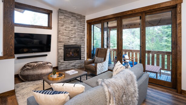 A modern living room with a fireplace, comfortable seating, and large windows offering a view of the outdoors.