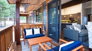 A spacious living area with a wooden deck, a sofa, a dining table, and a kitchen in the background.