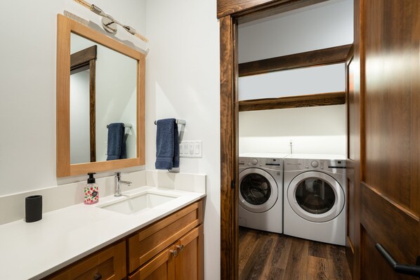 A bathroom with a wooden vanity, a sink, a mirror, and a washing machine.