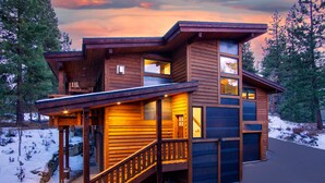 A modern log cabin with a wooden exterior, a covered porch, and a staircase leading to the entrance.