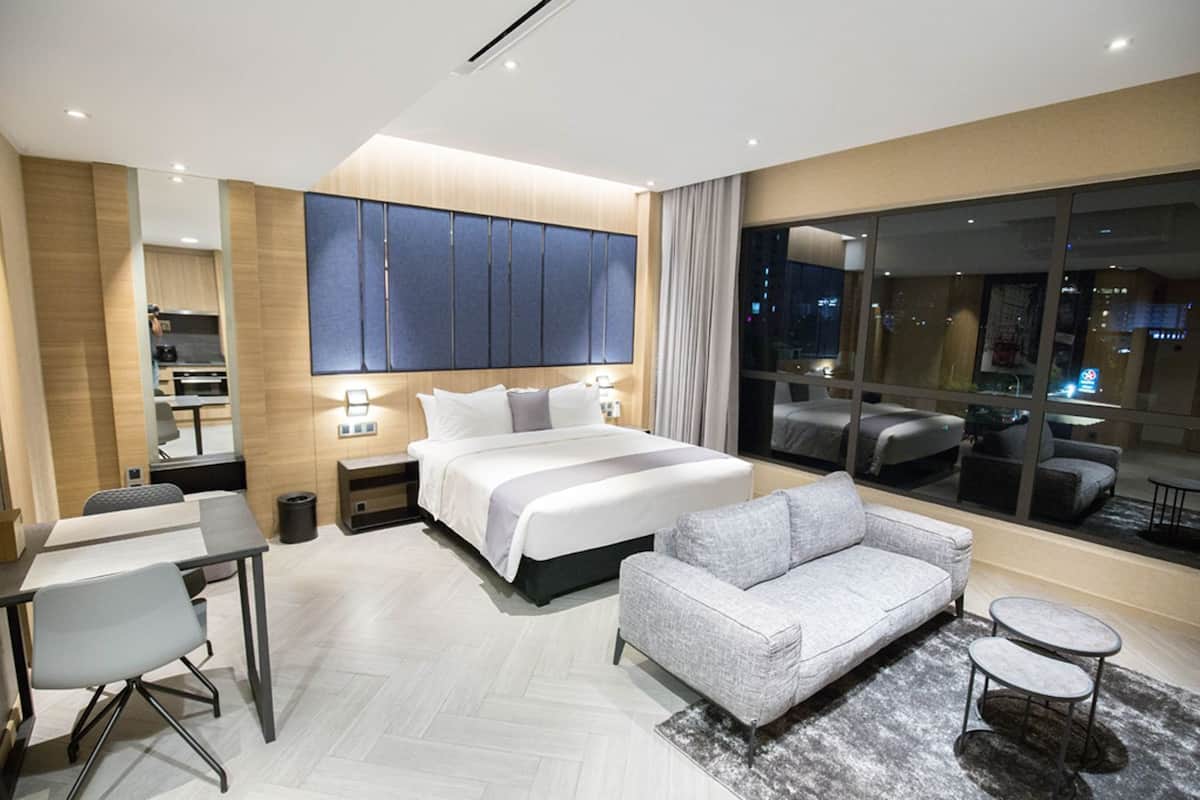 A modern hotel room with a large bed, a sofa, a desk, and a view of the city at night.