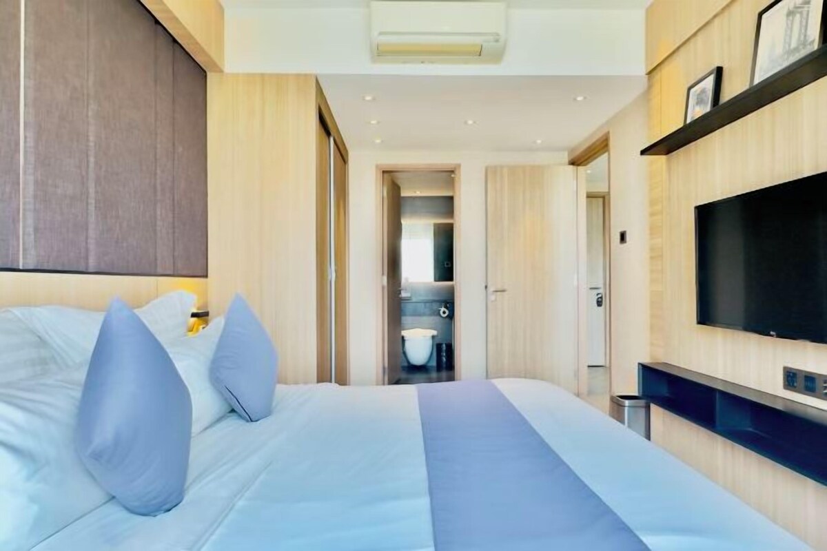 A modern hotel room with a large bed, a television, and a bathroom visible through an open door.