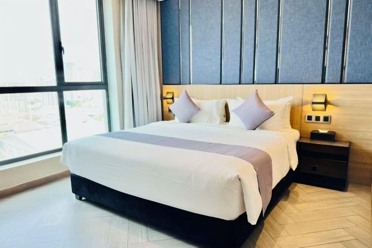 A hotel room with a large bed, bedside lamps, a nightstand, and a view through a large window.
