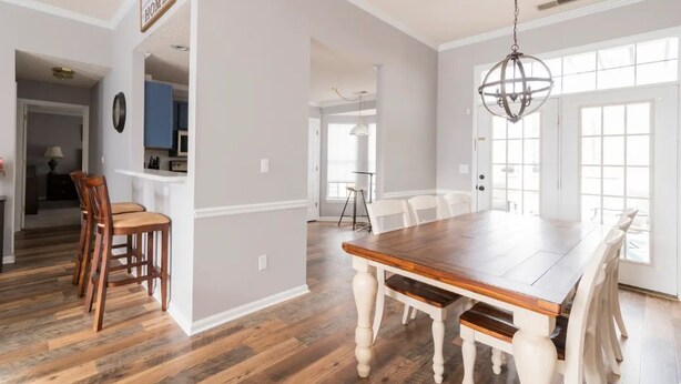A spacious dining area with a wooden table and white chairs, a chandelier, and a view through large windows. - Few Mins to Ballantyne-Pet Friendly-1 Level Home-Private Plunge Pool in Backyard (Pineville)