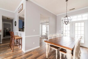 A spacious dining area with a wooden table and white chairs, a chandelier, and a view through large windows. - Few Mins to Ballantyne-Pet Friendly-1 Level Home-Private Plunge Pool in Backyard (Pineville)