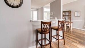 A dining area with two wooden chairs, a wooden dining table, and a wall-mounted clock. - Few Mins to Ballantyne-Pet Friendly-1 Level Home-Private Plunge Pool in Backyard (Pineville)
