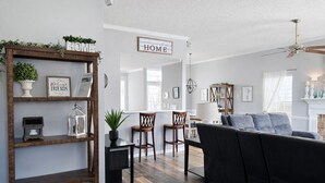 A modern living room with a black sofa, wooden chairs, and a bookshelf. There is a sign that reads "HOME" on the wall. - Few Mins to Ballantyne-Pet Friendly-1 Level Home-Private Plunge Pool in Backyard (Pineville)