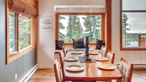 A dining area with a wooden table set for four, large windows offering a view of trees and a lake, and a sign on the wall that reads "Life is meant for Good & Great."