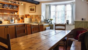 A kitchen with wooden cabinets, a wooden dining table, and a window with curtains. - Perfect for couples and familes to come and enjoy the local area. (Minehead)